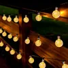 A string of solar-powered LED lights with round, textured bulbs is draped across a wooden fence. Voir les images du produit