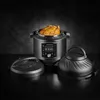 An Instant Pot Duo Crisp Multikocher with a roasted chicken inside, along with two detachable lids, is displayed on a dark surface against a dark, textured background. Produktbild-Vorschau