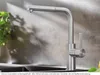 A stainless steel kitchen faucet with a pull-out spout is shown in a kitchen setting, with a plant in the background. Produktbild-Vorschau