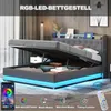 A modern grey upholstered bed frame with the mattress lifted to reveal storage space underneath. The bed frame has integrated RGB LED lighting around the base. Produktbild-Vorschau