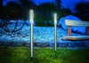 Two solar garden lights are illuminated at dusk in a garden setting with a bench and rocks. Produktbild-Vorschau