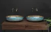 Two blue and gold sinks on a wooden vanity against a black wall. Produktbild-Vorschau