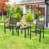 Two black metal chairs and a small black table are set up on a green lawn in front of a house with large windows. Produktbild-Vorschau