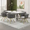 A dining room set with a white table and six gray chairs with gold legs, arranged on a patterned rug. Produktbild-Vorschau