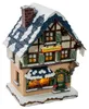 Ein Miniaturhaus mit schneebedecktem Dach und einem Schild mit der Aufschrift Zuckerbäckerei strahlt durch die erleuchteten Fenster eine gemütliche Atmosphäre aus während ein Kranz die grüne Tür schmückt und der Schornstein aus dem Dach ragt Produktbild-Vorschau