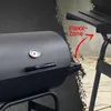A close-up view of a black charcoal grill with a thermometer on the lid. A red arrow points to a shelf on the side of the grill, labeled 'FlexX-Zone'. The background is a textured gray wall and a stone patio. Voir les images du produit