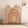 A wooden cabinet with a rainbow design is displayed in a room with a rug and basket. Náhled obrázku produktu