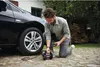A man is kneeling next to a car, using a portable air compressor to inflate the car's tire. Produktbild-Vorschau