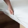 A hand is shown tucking a white fitted sheet onto a mattress. Náhľad obrázku produktu