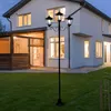 A black metal LED solar candelabra stands in a green lawn in front of a white house at dusk. Produktbild-Vorschau