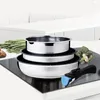 A set of stainless steel pots and pans with a detachable handle, placed on a stovetop with some vegetables in the background. Voir les images du produit