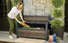 A woman is placing a wooden plank into a storage bench in a garden setting. Produktbild-Vorschau
