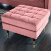 A close-up shot of a pink velvet ottoman with gold and black metal legs, placed on a dark wooden floor. Produktbild-Vorschau