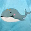 A close-up of a cartoon whale embroidered on a blue, fuzzy blanket. Produktbild-Vorschau