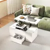 A white coffee table with a lift-top is shown in a living room setting next to a green sofa. The table has storage compartments and a drawer that is partially open, revealing headphones and other items. A laptop and a plate of waffles are on the lifted tab Podgląd zdjęcia produktu