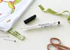A white Faber-Castell laundry marker with its black cap, a green ribbon, sewing pins, a fabric tag with 'MADE BY MARIA' written on it, and scissors are arranged on a white surface next to a white fabric with a colorful hummingbird design. Produktbild-Vorschau