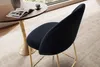 A close-up view of a black velvet bar stool with gold legs, placed next to a round wooden table with a magazine and a cup of coffee on it. Voir les images du produit