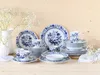 A collection of blue and white patterned porcelain dinnerware is arranged on a light wooden surface, with delicate white flowers in the background. Náhľad obrázku produktu