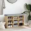 A shoe bench with storage compartments filled with shoes, placed in a room with a plant and a hanging garment. Anteprima dell’immagine prodotto
