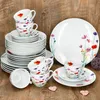 A set of white porcelain dinnerware with a floral pattern, arranged on a wooden surface. Produktbild-Vorschau