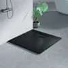 A black square shower tray with a stone-like texture is placed on a tiled floor in a bathroom setting. A shower head is visible on the wall, and a potted plant is in the background. Náhled obrázku produktu