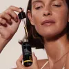 A woman is holding a bottle of beauty oil and a dropper. Podgląd zdjęcia produktu