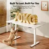 A white standing desk with large gold letters spelling '70KG' on top, and a cat reaching up towards the desk. Produktbild-Vorschau