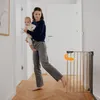 A woman is holding a baby and walking past a baby gate in a hallway. Voir les images du produit