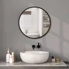 A modern bathroom vanity with a round mirror above a white vessel sink. The mirror reflects a bathtub and tiled wall. Produktbild-Vorschau