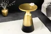 A gold and black side table with a decorative lotus on top, placed on a white rug next to a vase with branches and a sofa. Produktbild-Vorschau