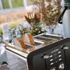 A toaster with bread slices in it, set on a table outdoors with greenery in the background. Produktbild-Vorschau