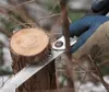 A hand wearing a blue glove is using a saw to cut a tree branch. Produktbild-Vorschau