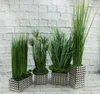 A collection of four decorative planters with artificial plants arranged against a white brick wall. Produktbild-Vorschau