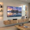 A modern living room with a wall-mounted TV displaying a landscape image, a wooden media console, and shelves. Podgląd zdjęcia produktu