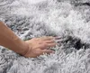 A hand is pressing into a soft, shaggy rug with a gradient of light gray to white. Podgląd zdjęcia produktu