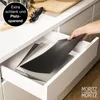 A hand is placing a black cutting mat into a kitchen drawer, where other cutting mats are already stored. Produktbild-Vorschau