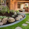 A landscaped garden with a curved rattan-effect border separating a flower bed from a lawn and stepping stones. Produktbild-Vorschau