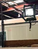 A work light is clamped to a metal bar in what appears to be a workshop or construction site. Podgląd zdjęcia produktu