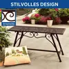 A metal garden bench with ornate scrollwork is placed on a patio next to a decorative pillow and potted plants. Náhľad obrázku produktu