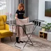 A woman is hanging laundry on a drying rack in a room. Produktbild-Vorschau