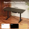 A dark standing desk with dimensions labeled, shown in a room with wooden floors and a plant. Produktbild-Vorschau