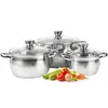 A set of three stainless steel pots with glass lids, arranged in front of a white background. Vegetables like zucchini, tomatoes, and onions are placed in front of the pots. Produktbild-Vorschau