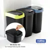 Three recycling bins with different colored lids are shown, with a close-up inset of a hand applying a sticker to a smaller bin lid. Produktbild-Vorschau