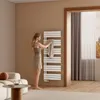 A woman is hanging a towel on a white towel radiator in a modern bathroom. Produktbild-Vorschau