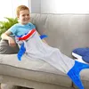 Lächelnder Junge auf einem grauen Sofa, eingehüllt in eine grau-blaue haifischförmige Decke mit offenem Mund-Design Produktbild-Vorschau