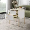 A round white side table with gold legs and handles, featuring two open drawers, is placed in a living room setting next to a green sofa. A vase of flowers and some books are on top of the table. Anteprima dell’immagine prodotto