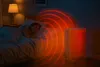 A woman sleeps in a bed next to a white oil radiator emitting heat waves. Podgląd zdjęcia produktu