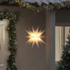 A white star-shaped LED Christmas decoration hangs outside a house, adorned with Christmas garlands and lights. Produktbild-Vorschau
