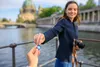 A woman is handing a memory card to someone off-camera, with a city skyline and river in the background. Produktbild-Vorschau