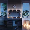 A vanity table with LED lighting and a stool in a room at night, with views of mountains and city lights through the windows. Produktbild-Vorschau